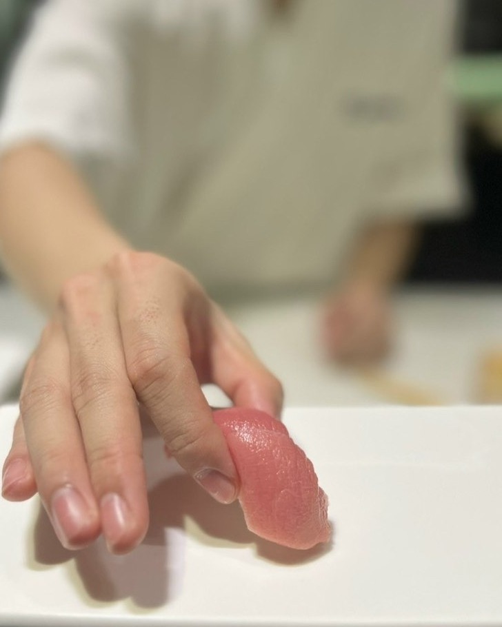 A chef's hand placing a piece of chutoro maguro sushi on a white plate.
