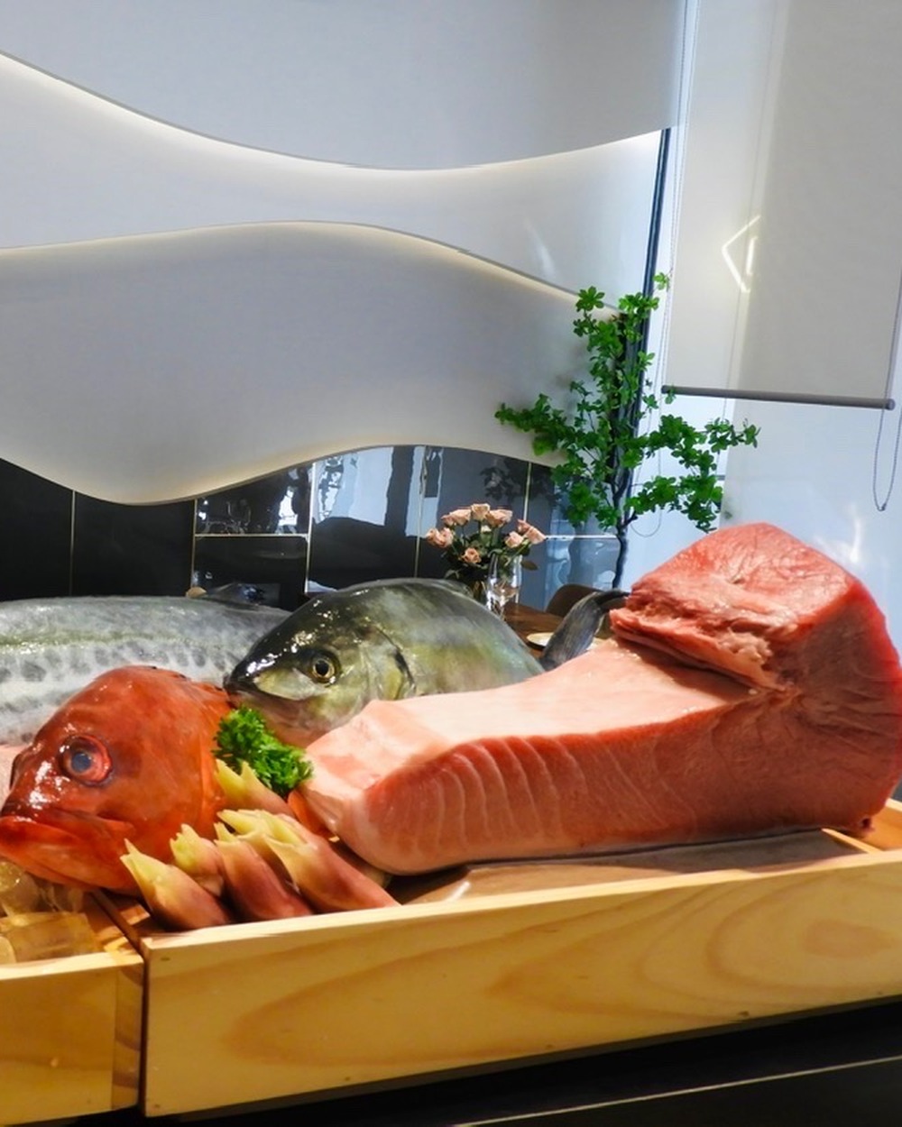 A spread of whole market fish and a block of tuna, arranged on wooden trays.