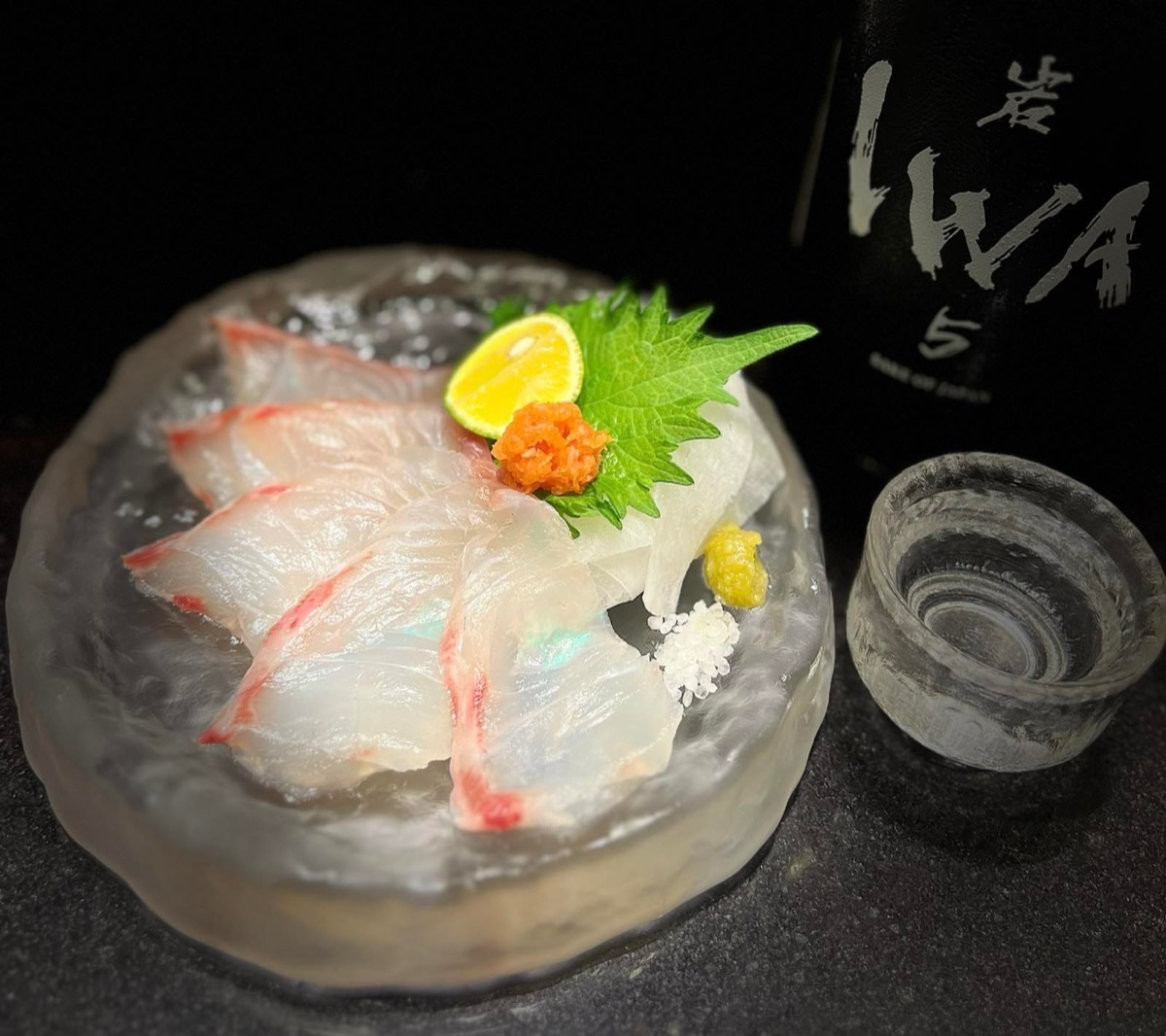 Halibut sashimi served on a block of ice with sake, garnished with shiso, citrus and ikura.