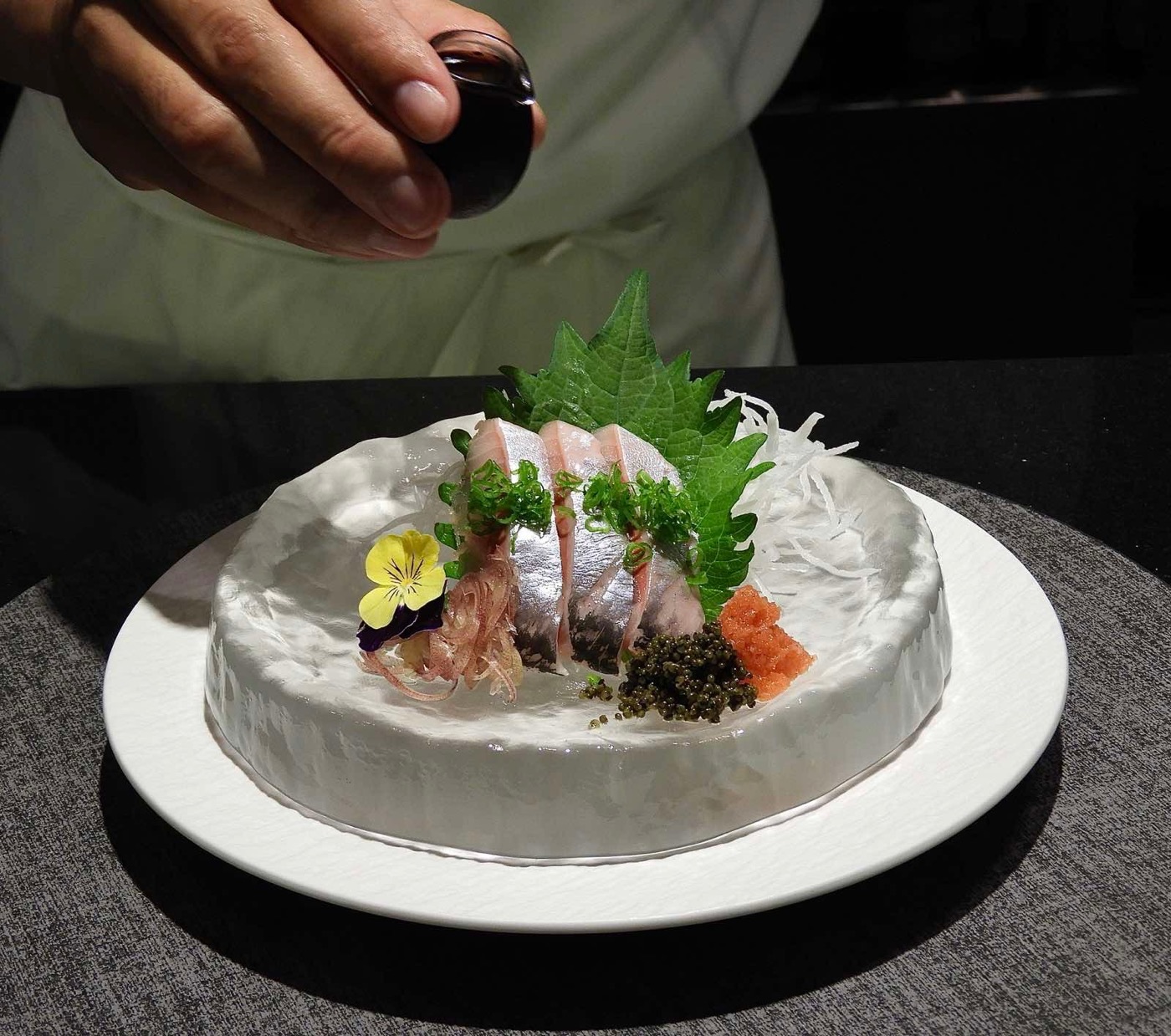 A chef pouring sauce over halibut sashimi plated on ice.