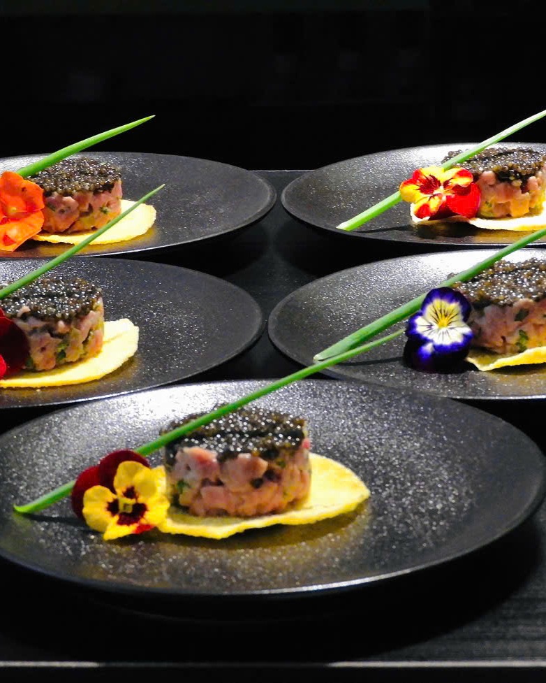 Five plates of wagyu tartare, each finished with a single edible flower.